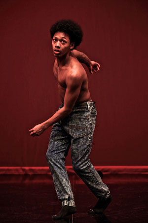A young African American male twists on a stage with a red background