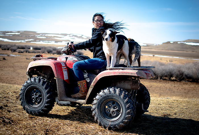 University of Montana journalism student Jordynn Paz looks back over her shoulder while operating an ATV with two dogs on the back